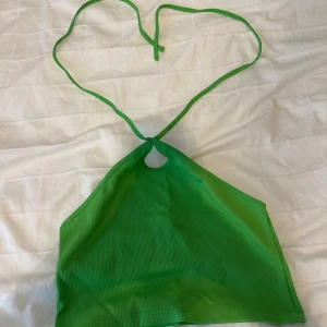 Grön ribbad halterneck topp från Zara - Snygg grön ribbad halterneck topp från Zara med knyt i nacken och liten cutout framtill. Toppen är ärmlös och croppad, perfekt för en trendig look. Materialet är stretchigt och mjukt, vilket gör den superbekväm att bära.