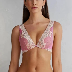 Rosa spets bralette med blommönster - Supersöt rosa bralette med krämvit spets och blommiga detaljer. Djup v-ringning och breda axelband med spets för extra snygg look. Perfekt att ha under en öppen skjorta eller som statement-plagg. Mjuk och bekväm känsla.
