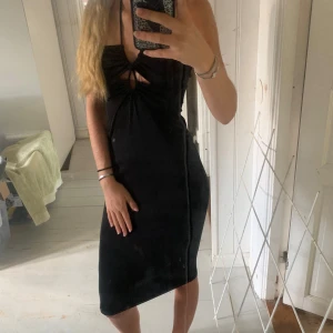 Svart tight halterneck klänning - Säljer en svart, tight halterneck klänning med snygg knytning i nacken och cut out-detalj framtill. Klänningen är figurnära och slutar strax under knäet, perfekt för dig som vill ha en stilren och trendig look.