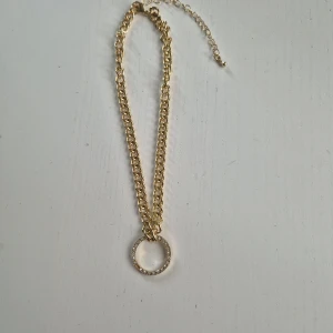Guldfärgat halsband med cirkelhänge - Stilrent halsband i guldfärg med grov kedja och ett runt hänge dekorerat med små glittrande stenar. Perfekt statement-piece för att lyfta din outfit. Justerbar längd för bästa passform. Skriv gärna vid frågor, priset kan diskuteras!🤗