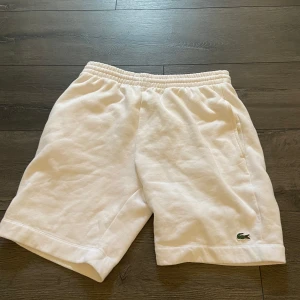 Vita shorts från Lacoste  - Snygga vita shorts från Lacoste i mjuk bomull med elastisk midja och klassisk krokodil-logga framtill. Regular fit med fickor på sidorna och en bakficka. Perfekta för chill dagar eller sportiga outfits.