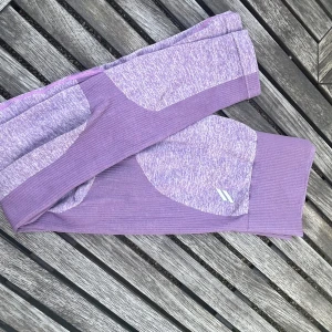 Doyoueven leggings  - Säljer ett par lila sömlösa leggings med ribbade detaljer och melerad look. De är stretchiga och sitter tight, perfekta för träning eller chill. Snygg design med olika nyanser av lila och diskret logga på benet.