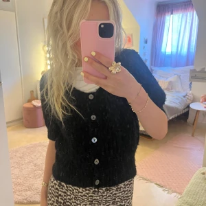 Svart stickad kofta från Lindex XS - Kort svart stickad kofta från Lindex i storlek XS. Koftan har grovstickad struktur, korta ärmar och knäpps med sex knappar framtill. Perfekt att slänga över en topp för en chill och snygg look.