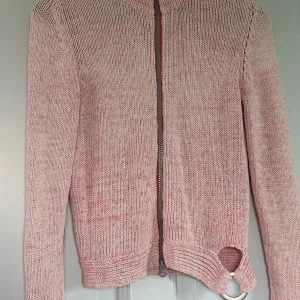 Rosa stickad kofta från Viriato - Säljer en rosa stickad kofta från Viriato med lång ärm och hel dragkedja framtill. Koftan har en unik detalj med en stor metallring vid nederkanten. Perfekt för dig som gillar att sticka ut med coola detaljer och mjuka material.