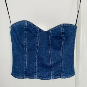 Jeans korsett-topp med dragkedja - Snygg jeansblå korsett-topp med markerade sömmar. Toppen har en söt hjärtformad urringning och dragkedja bak för enkel påklädning. 