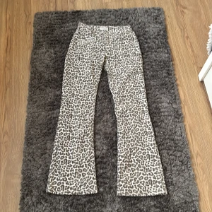 Leopardmönstrade bootcut lowwaste jeans - Säljer ett par snygga bootcut jeans utan fickor där bak men två fickor där fram med leopardmönster i beige och grå toner. Jeansen har en klassisk passform med utsvängda ben och midja. Perfekta för dig som vill sticka ut med ett djurmönster och cool siluett.