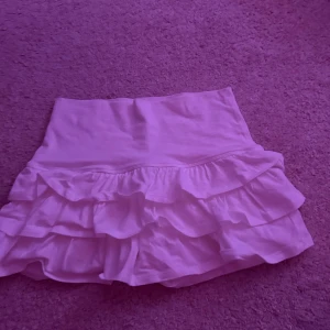 Vit volangkjol med låg midja - Supersöt vit kortkjol med flera volanger och låg midja med inbyggnad shorts. Kjolen är i mjukt bomullstyg och har en flowy känsla som ger en lekfull look. Perfekt för dig som gillar romantiska vibes och vill sticka ut lite extra.
