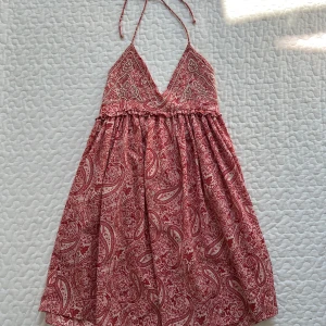 Röd rosa paisleymönstrad Zara klänning - Supersöt kort röd rosa klänning med paisleymönster och pärldetaljer på bysten. Knyt i nacken och v-ringad urringning. Lätt och luftig modell. Storlek S. Klänningen har en liten sminkfläck på insidan, syns inte när man har på sig den!! Skriv för frågor <3