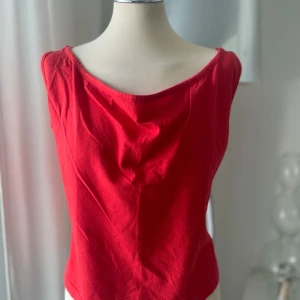 Röd ärmlös linnetopp med korsad rygg - Snygg röd linnetopp med breda axelband och coolt korsad detalj i ryggen. Toppen har en något lös passform och är perfekt för varma dagar. Tillverkad i mjuk bomull som känns skön mot huden.