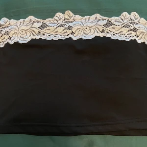 Svart bandeau tubtopp med spets SHEIN stl L  - Oanvänd Svart bandeau tubtopp från SHEIN i storlek L. Toppen har en snygg vit spetskant upptill som ger en romantisk vibe. Perfekt att styla med höga jeans eller kjol för en trendig look. Mjuk och stretchig syntetblandning som sitter skönt mot kroppen.