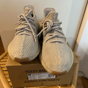 Adidas Yeezy Boost 350 V2 i SESAME *DEADSTOCK* - Säljer ett helt nytt par Adidas Yeezy Boost 350 V2 i en snygg beige färg. Skorna har stickad ovandel, snörning och den ikoniska ribbade sulan i ljus ton. Perfekta för dig som gillar streetwear och vill ha något unikt på fötterna.