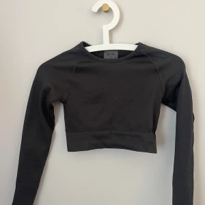 Grå ribbad croppad topp Aim'n - Grafitgrå ribbad långärmad sport topp från aim’n,  tight med stretchigt tyg, passar xs-xxs. Hittar inte den på deras sida längre så kan inte se nypris men säljer för 100kr💗