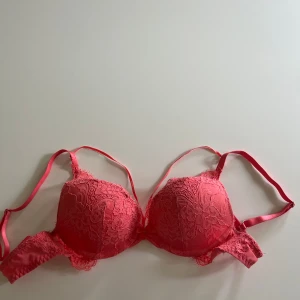 Korallfärgad spets-bh från Hunkemöller - Snygg rosa bh från Hunkemöller med vadderade kupor och spetsdetaljer. Justerbara axelband, går att ta bort banddetaljerna över bysten, klassisk knäppning bak. Storlek 70A. Använt 1 gång för ett år sedan, finns ej att köpa i butik/webbsida längre🩷Nypris 429kr💕