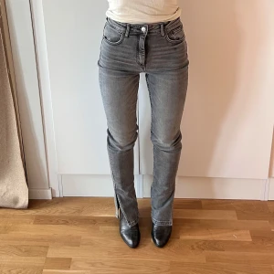 Grå jeans med slits - Snygga grå jeans från Zara med hög midja och raka ben. Jeansen har en cool slits nertill på benen. Tillverkade i denim med en lätt tvättad look som ger en trendig vibe. Jag har aldrig annt de eftersom de är för långa för mig (jag är 158cm, o behövde ha ca 6cm klackar på bilderna). Storlek 36 men de är små i storleken o sitter mer som en 34!