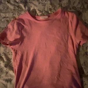 Rosa basic t-shirt från Gina Tricot - En enkel rosa t-shirt från Gina Tricot, basically basics-kollektionen. T-shirten har rund halsringning och korta ärmar. Tillverkad i mjuk bomull som känns skön mot huden. Perfekt för en chill och avslappnad look.
