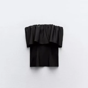 Svart volang tubtopp - Supersnygg svart tubtopp med volangdetalj upptill. Toppen är axelbandslös och har en bandeauformad passning som sitter tight mot kroppen. Perfekt att styla med lågmidjade byxor eller kjol för en trendig look. Använd några enstaka gånger. 