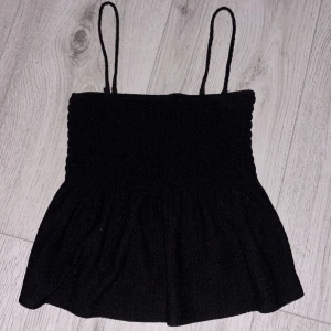 Svart smockad tubtopp Gina Tricot XS - Supersöt svart smockad tubtopp från Gina Tricot i storlek XS. Toppen har avtagbara tunna axelband och en volangig nederdel som ger en snygg siluett. 