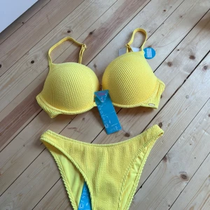 Gul push up bikini från Censored - Superfräsch gul bikini från Censored med push up-bh och vadderade kupor. Bikinin har en ribbad struktur och högt skurna trosor som ger en snygg siluett. Perfekt för strandhäng och poolparty. Materialet är mjukt och stretchigt syntet.