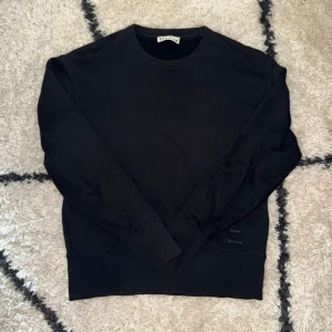 Acne studios tröja - Säljer en superfin och minimalistisk crewneck från Acne Studios i djupsvart färg. Ren design med diskret Acne Studios-broderi vid fållen, perfekt balans mellan modern lyx och enkelhet.  Tillverkad i 100 % premiumbomull, väldigt mjuk och hög kvalitet. Märkt storlek XS, men passar som en Small (något boxig/kort beroende på kroppsform).  Inga defekter, inga hål eller fläckar  Tidlös, stilren och funkar till allt 