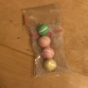 Sött pack med macaron-berlocker - Pack med fyra macaron-berlocker i pastellfärger: grön, rosa, gul och ljusrosa. Berlockerna är formade som små macarons. Perfekt accessoar för dig som gillar färgglada och unika detaljer.