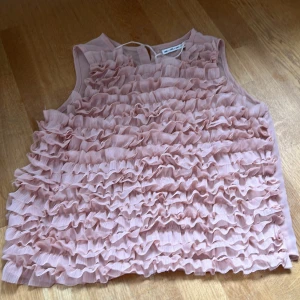 Rosa volangblus från UNIQ XS - Supersöt ljusrosa blus från UNIQ i storlek XS. Toppen är ärmlös och täckt av flera lager volanger framtill, vilket ger en riktigt romantisk och trendig look. Baksidan har knappar hela vägen och tyget är lätt och luftigt, perfekt för varmare dagar. Tror ej att den säljs längre och har sparsamt använts därav priset. Klicka EJ på köp nu och vid fler frågor skriv!❤️