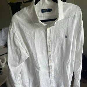 Vit linneskjorta från Polo Ralph Lauren XXL - Klassisk vit skjorta i linne från Polo Ralph Lauren i storlek XXL. Skjortan har lång ärm, knappar framtill och den ikoniska broderade loggan på bröstet. Perfekt för en clean och stilren look.