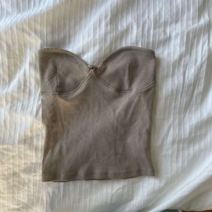 Beige ribbad bandeau tubtopp - Supersnygg beige bandeau tubtopp med ribbad struktur och formade kupor. Toppen är axelbandslös och har en clean, stilren look som passar perfekt till jeans eller kjol. Mjuk och stretchig för en bekväm passform.