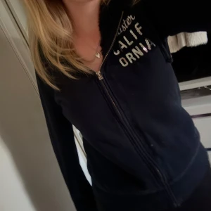 Marinblå zip hoodie från Hollister - Marinblå zip hoodie från Hollister med dragkedja framtill och broderad text i vitt och glittriga paljetter. Hoodien är fodrad!                                            Är i storlek M men passar S också!🩷                              Har liknande zip hoodies, kolla gärna in de! 