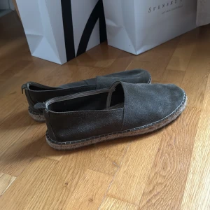 Mörkgrå mocka loafers från A Days march - Snygga loafers i mörkgrå mocka. Skorna har en klassisk, avslappnad design med rund tå och platt sula i repdetalj. Perfekta för en stilren och chill look under varmare dagar.