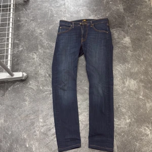 Mörkblå Lee Luke jeans W29 L32 - Snygga mörkblå jeans från Lee, modell Luke. De har smal passform, klassiska fem fickor och guldfärgade sömmar. Jeansen är tillverkade i bomull med lite stretch för extra komfort. Perfekta för dig som gillar en modern och stilren look. Priset kan förhandlas men eftersom nypriset ligger på ca 1200 så tycker jag att 550 är ett bra pris 