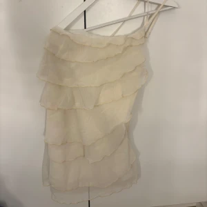 Champagnefärgad volangklänning - Supersöt kort klänning i champagnefärg med flera lager volanger och tunna justerbara axelband. Lätt och luftig känsla, perfekt för sommarens varma dagar. Ger en romantisk och trendig vibe med sitt flowiga tyg och feminina look.