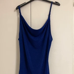 Glittrig blå kortklänning med snörning - Snygg glittrig sexig blå kortklänning med smala axelband och draperad urringning. Klänningen har snörning i sidan för en cool detalj och är figurnära. Passar perfekt för en night out till klubben, jätte fin och sexig, lyser så fint och materialet är bekvämt. Haft på mig den 1 gång bara 