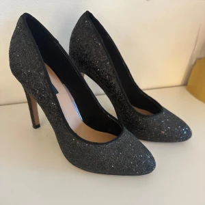 Svarta glittriga pumps från ONLY - Svarta pumps från ONLY med glittrig yta och spetsig tå. Insidan är beige och skon har en klassisk siluett. Köpta begagnade och aldrig använt själv pågrund av fel storlek (endast använda 2 gånger när dom köptes). Syns endast på undersidan att dom är använda. 