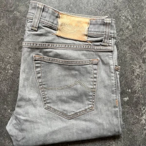 Grå jeans från Jacob Cohen, stl 34 - Snygga grå jeans från Jacob Cohen i klassisk femficksmodell. Jeansen har orange kontrastsömmar, silverfärgade nitar och knappar samt ljuslila detaljer på insidan. Tillverkade i mjuk bomullsdenim med en rak passform som funkar till allt. Säljer eftersom fe inte passade mig 