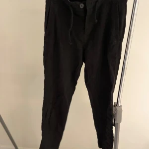 Svarta linnebyxor  - Snygga svarta byxor från Zara med snörning i midjan och knappstängning. Byxorna har en avslappnad passform och är perfekta för en stilren look. De har också bakfickor med knappar för extra stil och funktionalitet. Har du några frågor så bara hör av er! Pris kan diskuteras vid en snabb affär!