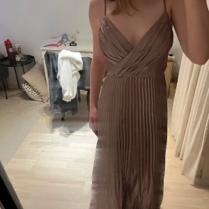 Rose/ljusrosa långklänning med omlott - Elegant beige långklänning med omlott-design och smala axelband. Klänningen har ett plisserat kjolparti som ger en fin rörelse och en v-ringad urringning framtill. Endast använd 1 gång och är i nyskick. Kom privat om du vill ha mer bilder!😁