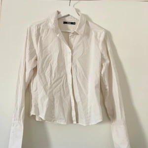 Vit långärmad skjorta - Säljer en klassisk vit långärmad skjorta. Skjortan har en enkel design med knappar framtill och en krage. Perfekt för en stilren look.