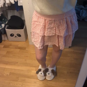 Rutig rosa kortkjol - Söt kortkjol i rosa och vitt med volanger. Kjolen har ett rutigt mönster. Från Kappahls barn avdelning! Tyvärr klippt bort lappen då den kliade..