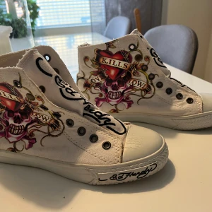 Vita sneakers med tryck från Ed Hardy, Love kills slowly. Strlk 36 - Unika vita sneakers från Ed Hardy med färgglada tryck av en dödskalle och en tiger. Skorna har snörning och Ed Hardy-loggan på sidan. Perfekta för dig som vill sticka ut med en cool och konstnärlig stil.