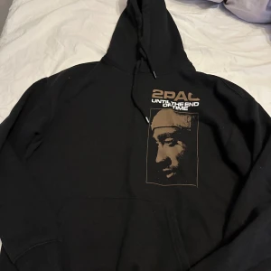 Svart hoodie med 2PAC-tryck, storlek S men är stor i storleken så den passar även M - Säljer en svart hoodie med stort 2PAC-tryck både fram och bak. 