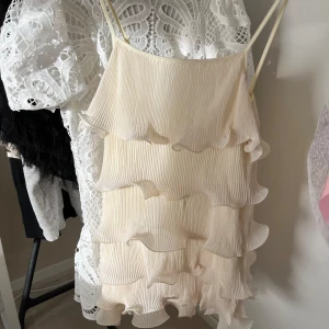 Klänning med volanger - Säljer en elegant champagnefärgad klänning med tunna axelband och flera lager av volanger. Storlek S men passar även XS. Endast andvänd en gång.