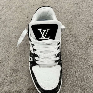 Svartvita sneakers från Louis Vuitton - Stilrena svartvita sneakers från Louis Vuitton med klassisk snörning och märkets logotyp på plösen. Skorna har en unik design med monogramdetaljer och en bekväm sula för optimal komfort.