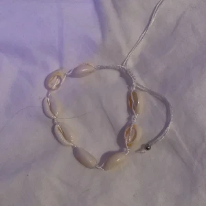 Vitt snäckarmband - Charmigt armband med vita snäckor trädda på en justerbar vit tråd. Perfekt för en strandig look eller sommarens äventyr. Snäckorna ger en naturlig och bohemisk känsla. Och man kan välja storlek på den.