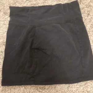 Svart kortkjol - Snygg svart kortkjol med en enkel design. Perfekt för en stilren look. Kjolen har en bred midja för extra komfort och en figurnära passform.