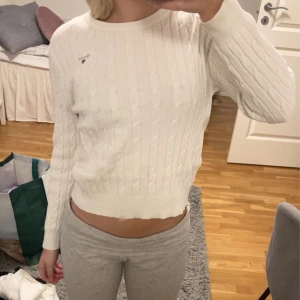 Vit stickad tröja från Gant - Säljer en stilren vit stickad tröja från Gant med kabelstickat mönster. Tröjan har långa ärmar och en rund halsringning. Perfekt för en klassisk och bekväm look.