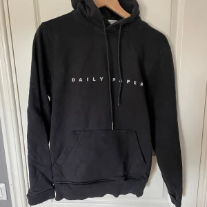 Svart hoodie från Daily Paper - Säljer en stilren svart hoodie från Daily Paper med vit logotyp på bröstet. Tröjan är perfekt för en avslappnad look. 