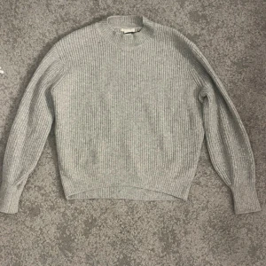 Grå ribbad stickad tröja XS - Säljer en stilren grå stickad tröja med ribbad struktur. Tröjan har en klassisk rund hals och långa ärmar, perfekt för kyligare dagar. Passar bra till både jeans och kjol. Från h&m i storlek XS