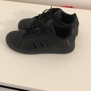 Svarta sneakers från Adidas - Säljer ett par stilrena svarta sneakers från Adidas. Skorna har en klassisk design med de ikoniska tre ränderna på sidan och snörning framtill. Perfekta för en casual look.