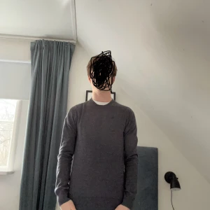 Grå tröja från J.Lindberg - Säljer den här snygga stickade grå tröja från J.Lindberg med rund halsringning. Perfekt för en stilren look. Tröjan har en diskret logga på bröstet och långa ärmar. 