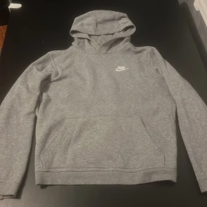 Grå hoodie från Nike - Säljer en stilren grå hoodie från Nike med broderad logga på bröstet. Tröjan har en klassisk känguruficka och en bekväm huva. Strl 158-170 motsvarar ungefär XS.